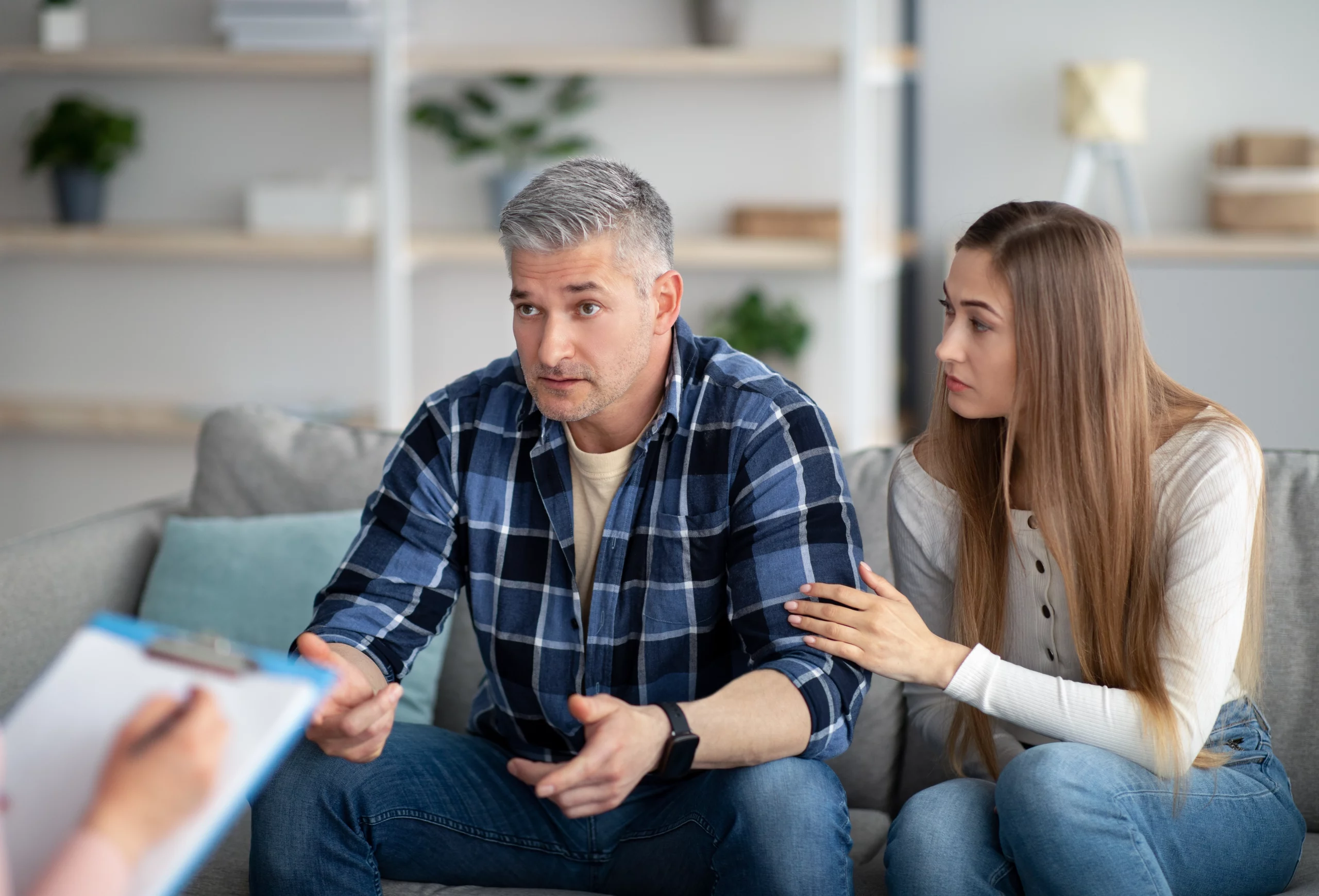 Concerned man discusses immigration issues with a therapist as a supportive woman sits beside him.