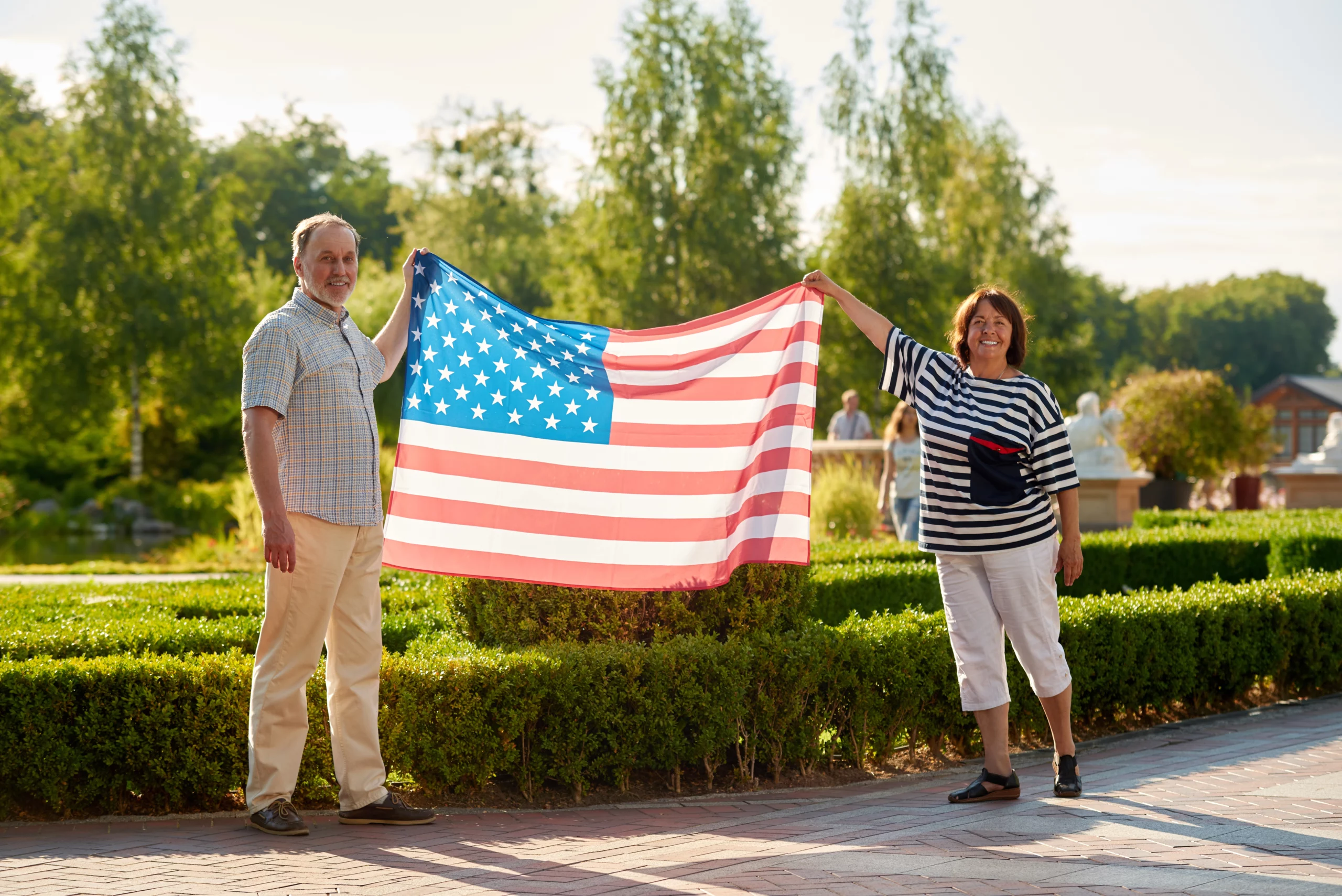 Man and woman holding American flag in sunlit park, symbolizing parental green card process in the U.S.