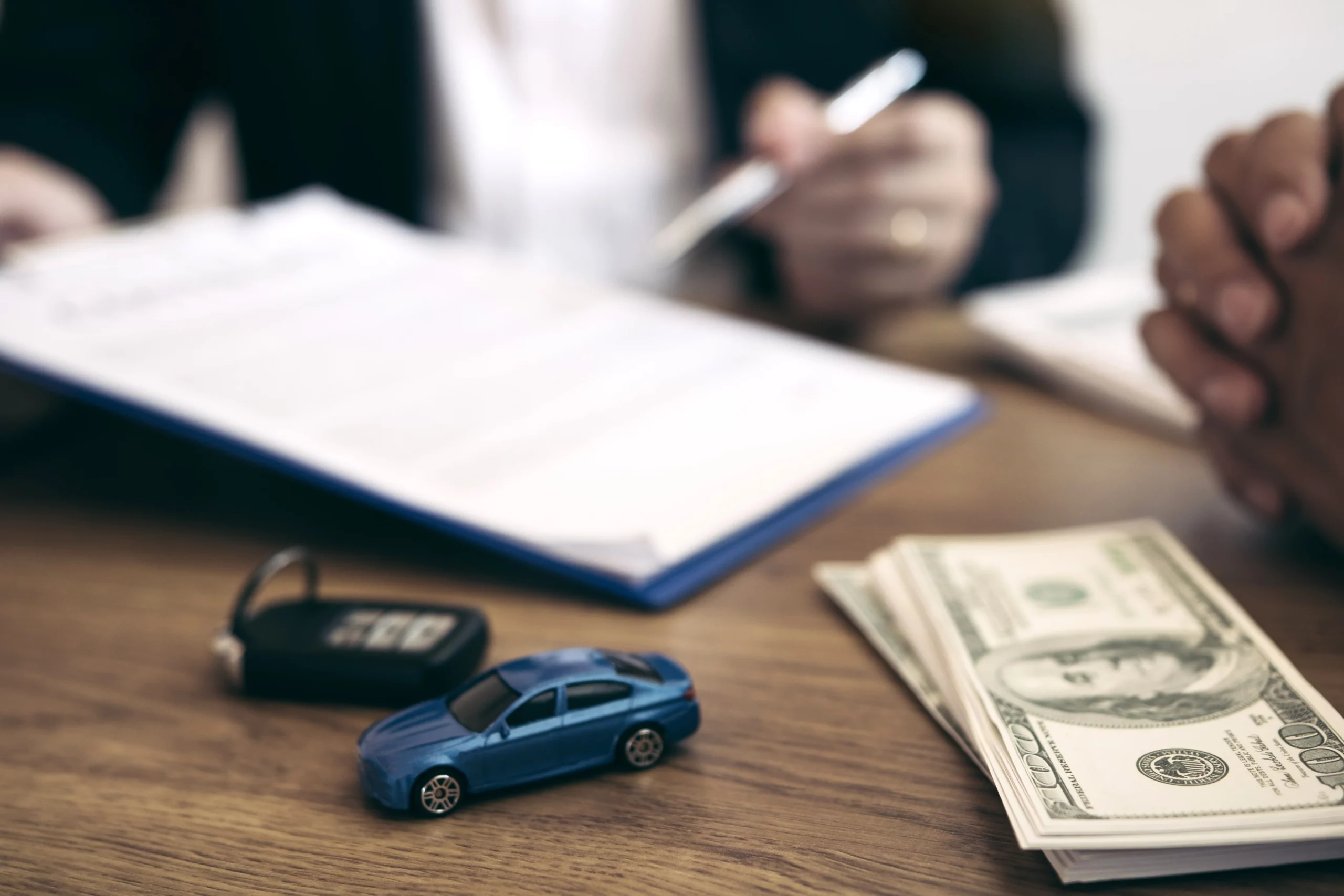 Close-up of toy car, key and money with people reviewing documents, illustrating concern about losing a car in Chapter 7 bankruptcy in North Carolina.